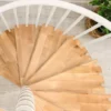 Vista superior de escalera de caracol con peldaños de madera clara, ideal para interiores pequeños y decoración minimalista.