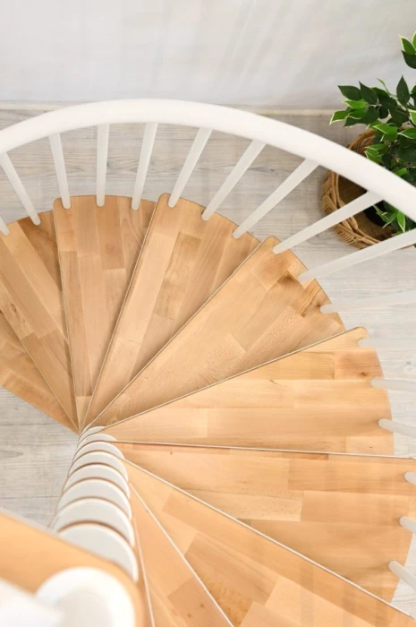 Vista superior de escalera de caracol con peldaños de madera clara, ideal para interiores pequeños y decoración minimalista.