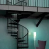 Escalera de caracol negra metálica en interior tipo loft, solución elegante para acceso a altillos en espacios modernos y bien iluminados
